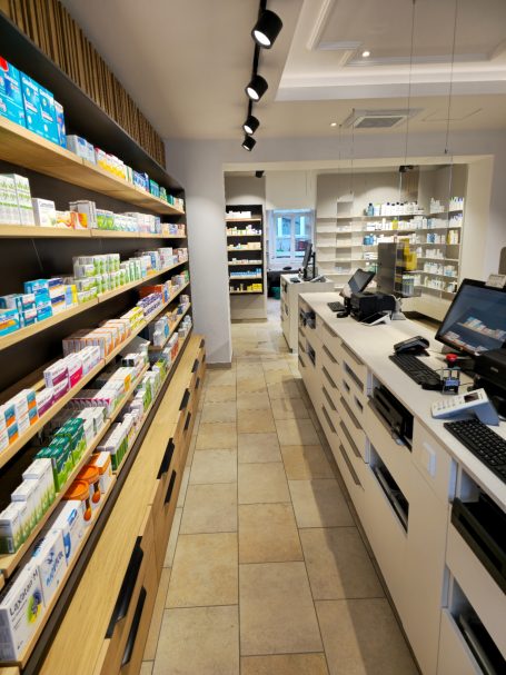 Innenansicht einer modernen Apotheke mit Regalen voller Medikamente und einem Verkaufsbereich.