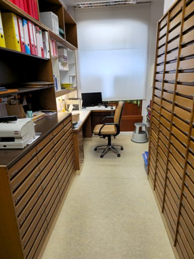 Büro mit Schreibtisch, Stuhl und Regalen in einer schmalen Gasse.