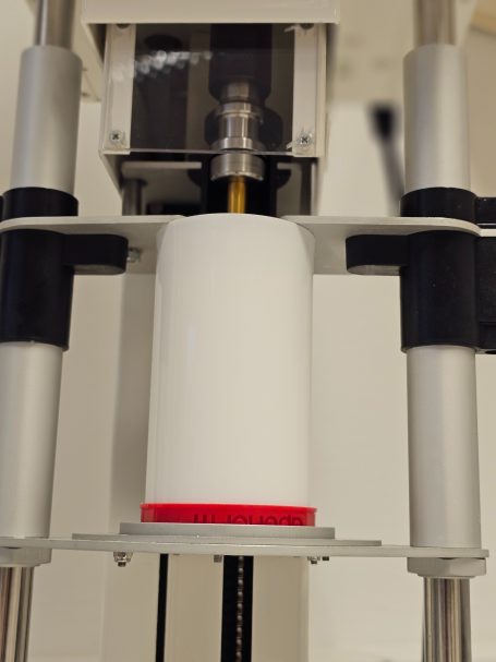 Eine weiße Zylinderform mit rotem Rand in einer Halterung.