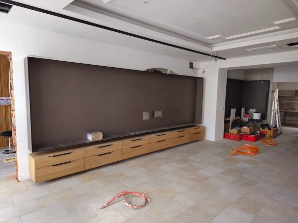 Raum mit einem langen Holzregal und unverputzten Wänden, Baustellenutensilien sichtbar.