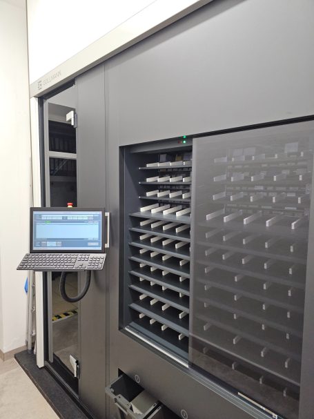 Automatisiertes Lagerregal mit Monitor und Fächern für Lagerwaren.