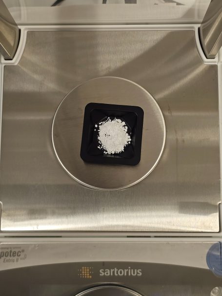 Weiße Substanz in einer kleinen Schale auf einer digitalen Waage.