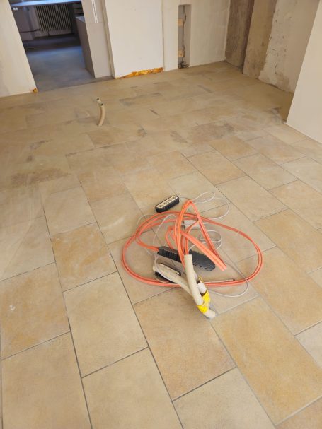 Ein leerer Raum mit neuen Fliesen, in der Mitte ein Kabel und Geräte liegen.
