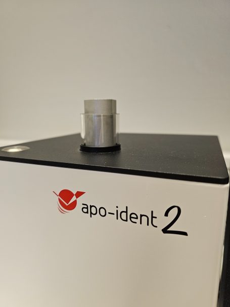 Silberne Kappe auf einem weißen Behälter mit dem Schriftzug "apo-ident 2".