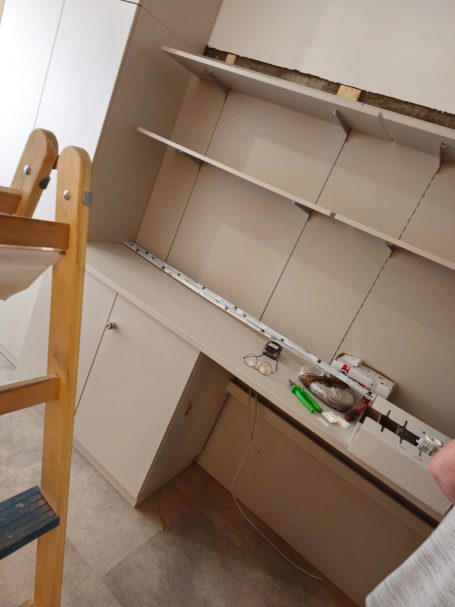 Ein unvollendeter Raum mit beige Wänden, Regalen und einem Arbeitstisch.